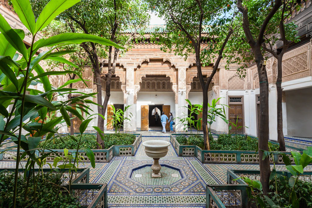 shutterstockRF_395031667.jpg A grand, tiled courtyard with a number of raised flower beds, from which large leafy trees grow.