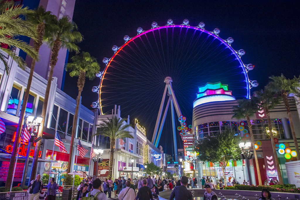 Visitors walk along the LINQ Promenade in Las Vegas at night with the High Roller ferris wheel in the background lit up in brightly coloured lights
