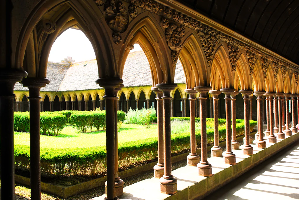 Cloisters, Abbaye du Mont St-Michel A row of arched stonework leading into an open square lawn