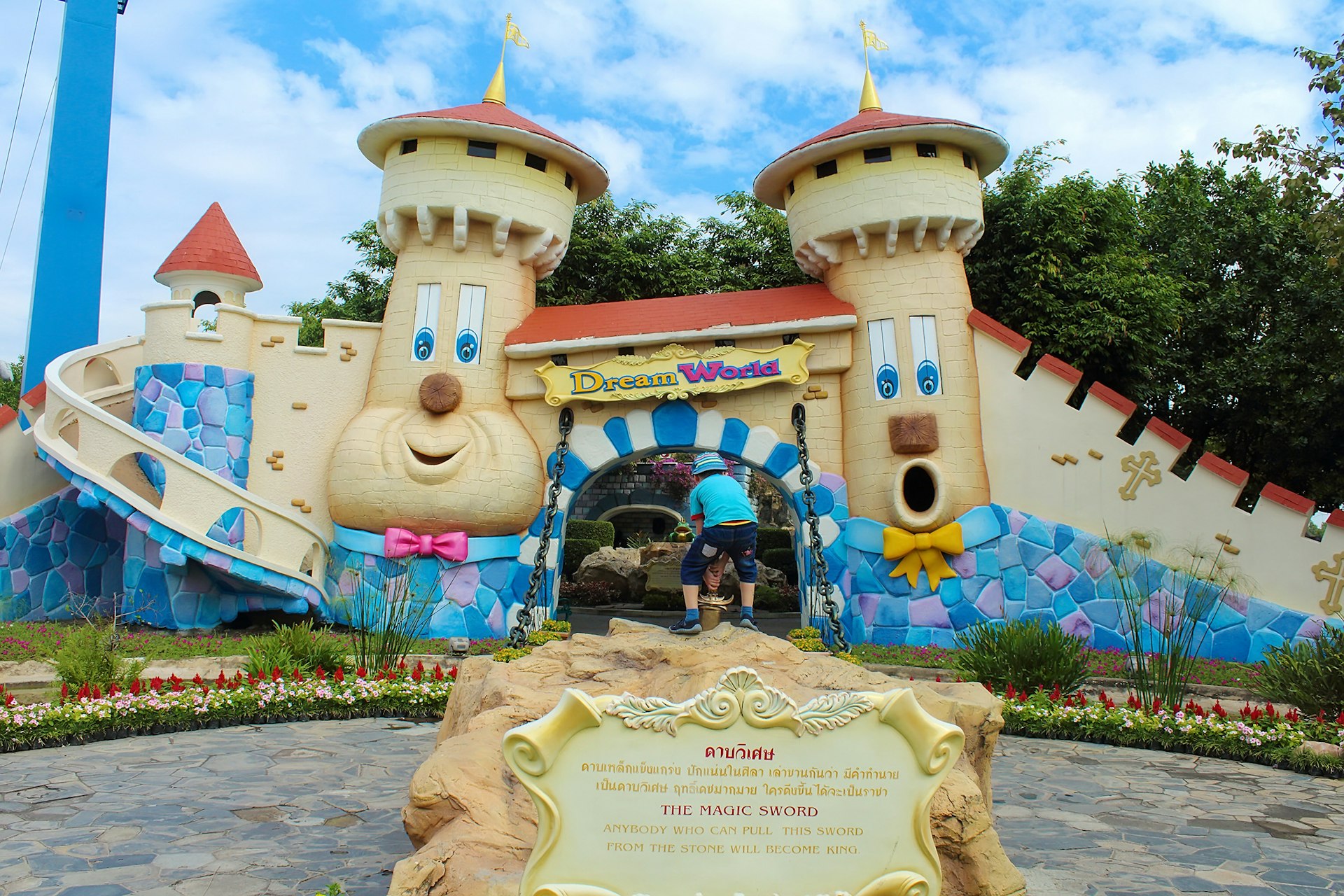 The entranceway to Dream World amusement park in Bangkok includes a large cartoon-ish castle with big smiling faces on them as a child gets ready to enter.