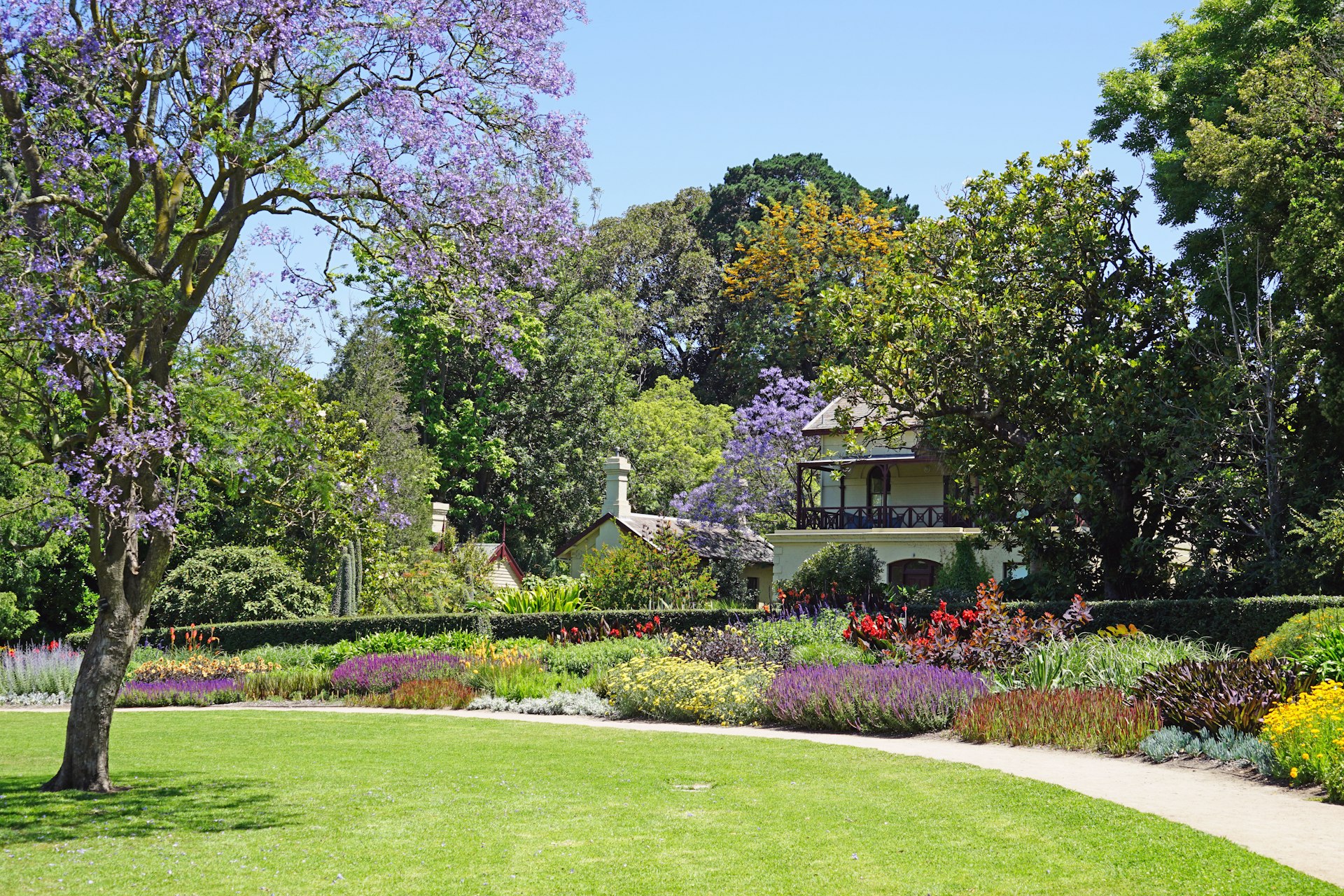 A view of a section of the Royal Botanic Gardens in Melbourne. A patch of green lawn is visible, beyond it are a number of colourful bushes and trees of various shapes and sizes.