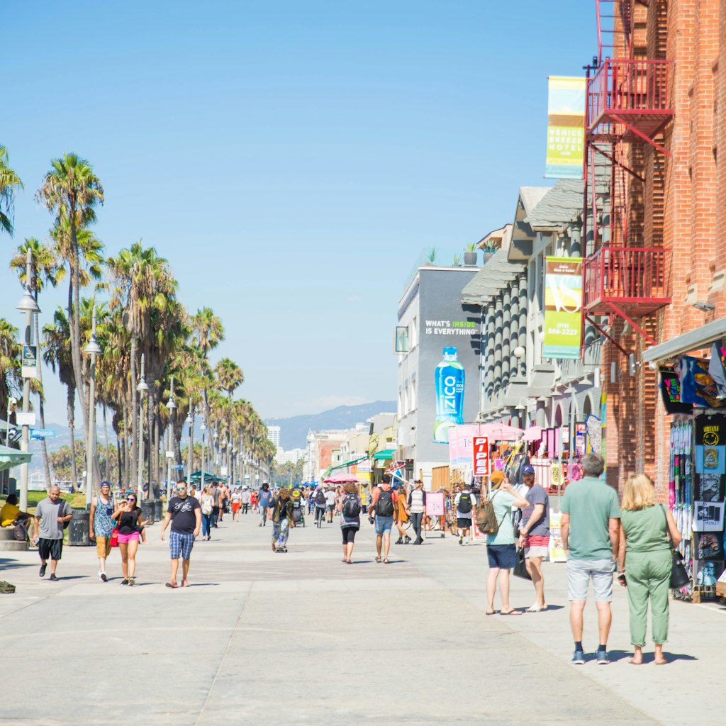 VENICE BEACH, USA - SEPTEMBER 29, 2016: The crowded Venice Beach Boardwalk. Lots of people are strolling down the boardwalk. On the sides there are several shops and palm trees.