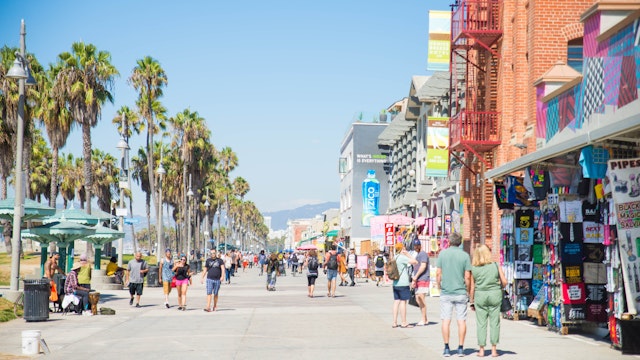 VENICE BEACH, USA - SEPTEMBER 29, 2016: The crowded Venice Beach Boardwalk. Lots of people are strolling down the boardwalk. On the sides there are several shops and palm trees.