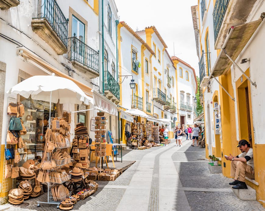Gatuvy av Evoras historiska centrum, Portugal.  Gatan är smal och kantas av stånd som säljer sina varor utanför.