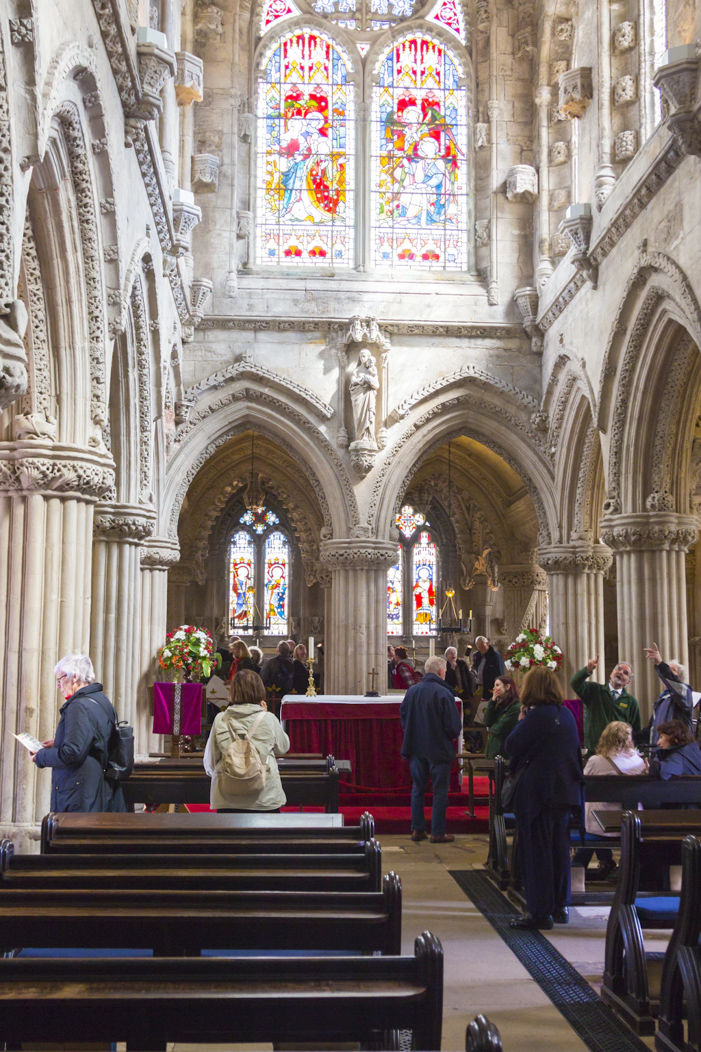 Rosslyn Chapel Visitors in pews at a chapel with ornate stained glass windows above them