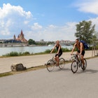 JULY 9, 2017: A young couple riding bicycles on Danube Island in the Donaustadt district. St. Francis of Assisi Church is in the background.