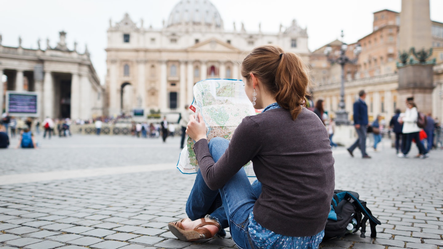 Pretty young female tourist studying a map at St. Peter's square in the Vatican City in Rome