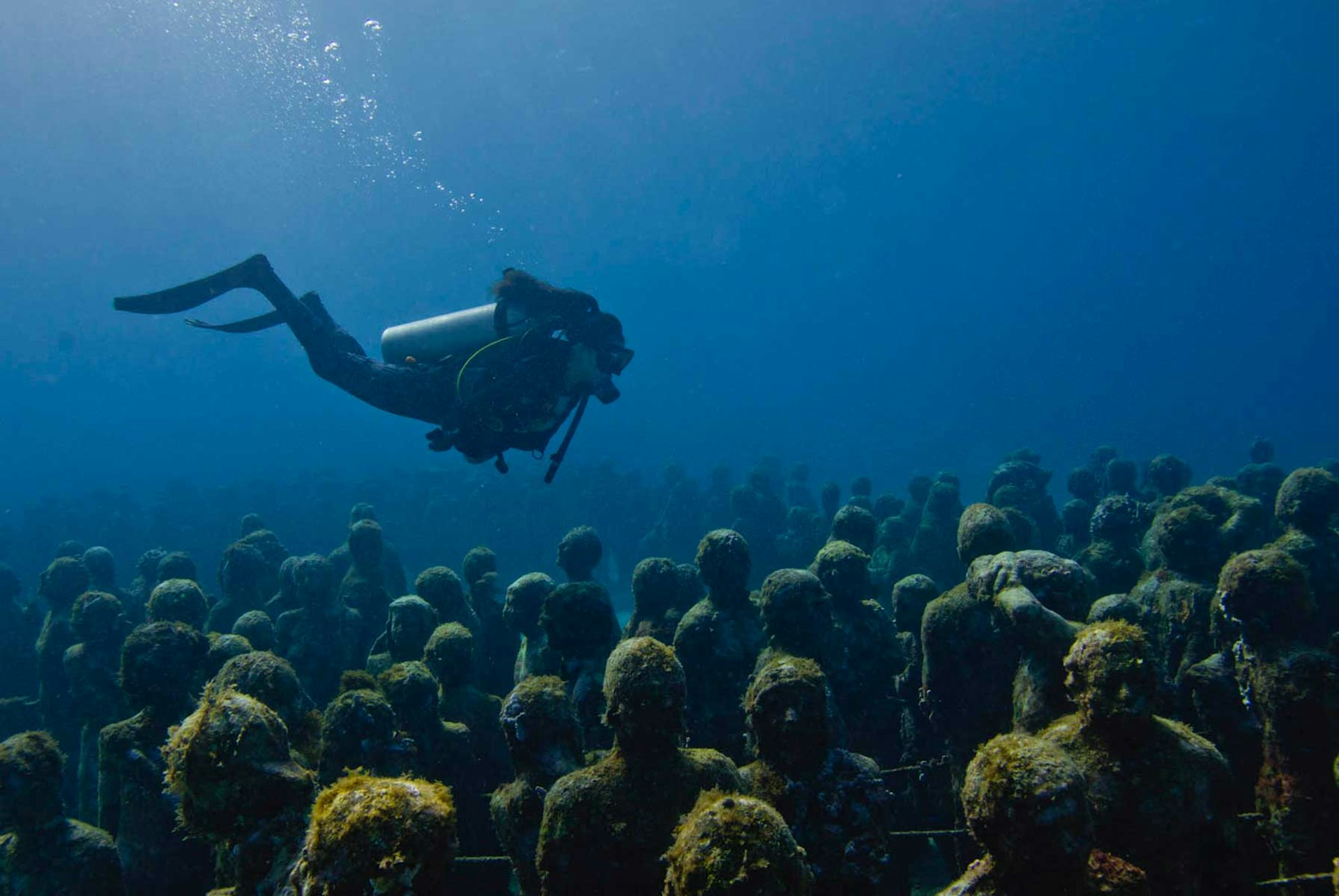 A diver swims above an underwater sculpture made up of many individual standing figures