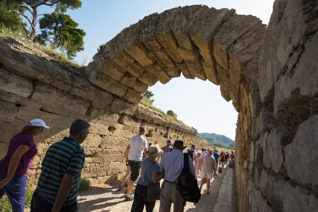 Crowds walk under a stone arched entrance into the stadium where Olympic events were originally held in Ancient Olympia, Greece.
