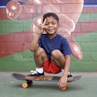 African American boy sitting on skateboard by urban mural