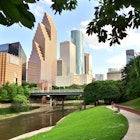 Wide shot of Houston's modern skyline and paved bicycle/walking path in Buffalo Bayou Park on a summer afternoon