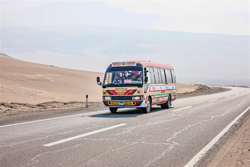 Bus travelling on Pan-american highway through Peru A bus travels on the Pan-America Highway through Peru. The bus is painted in bright colours and a few of the passengers are visible through the windows. The landscape around the bus is desert.