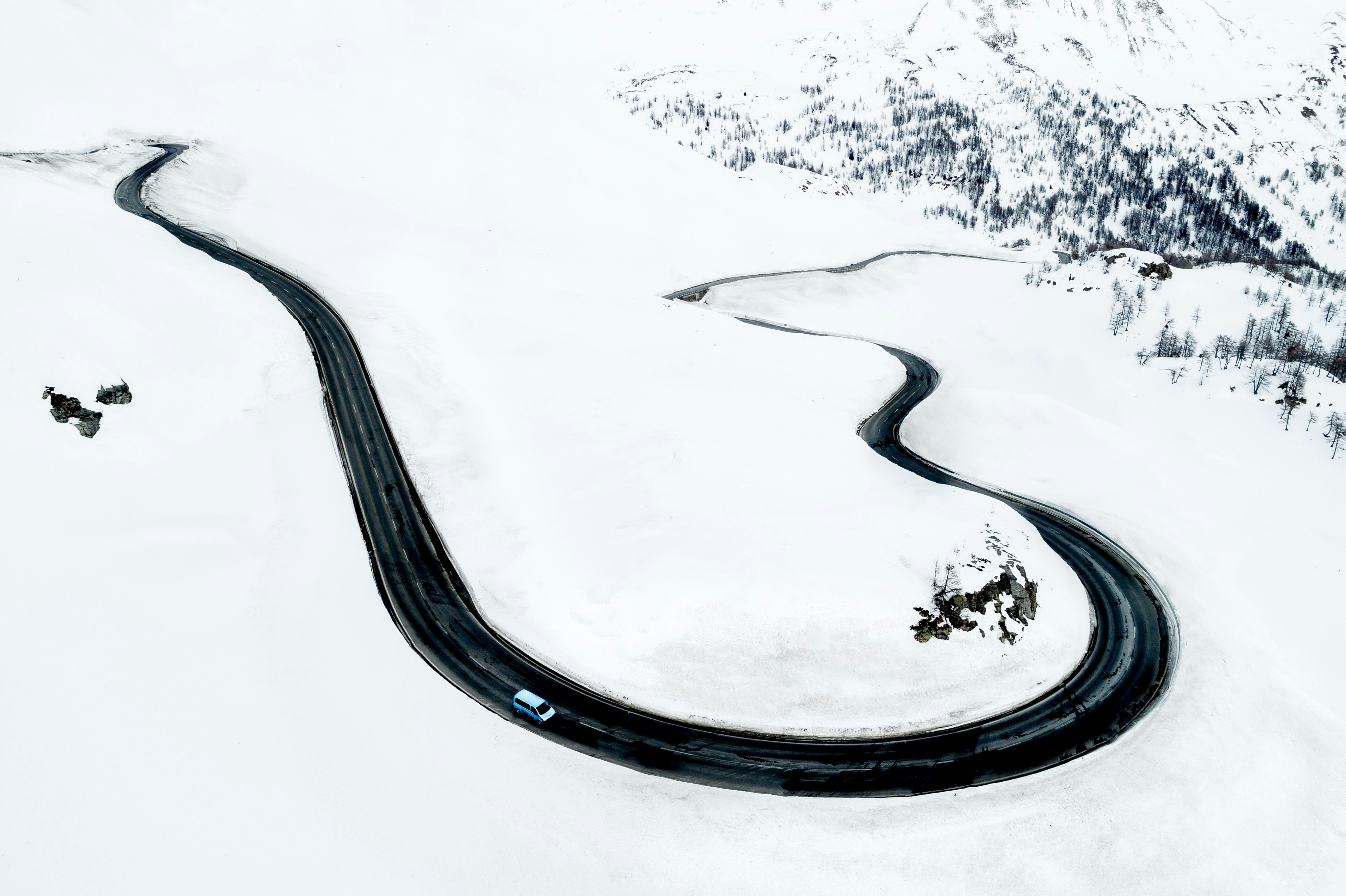 A car travels on a mountain road winding its way through a snowy landscape en route to St Moritz, Switzerland