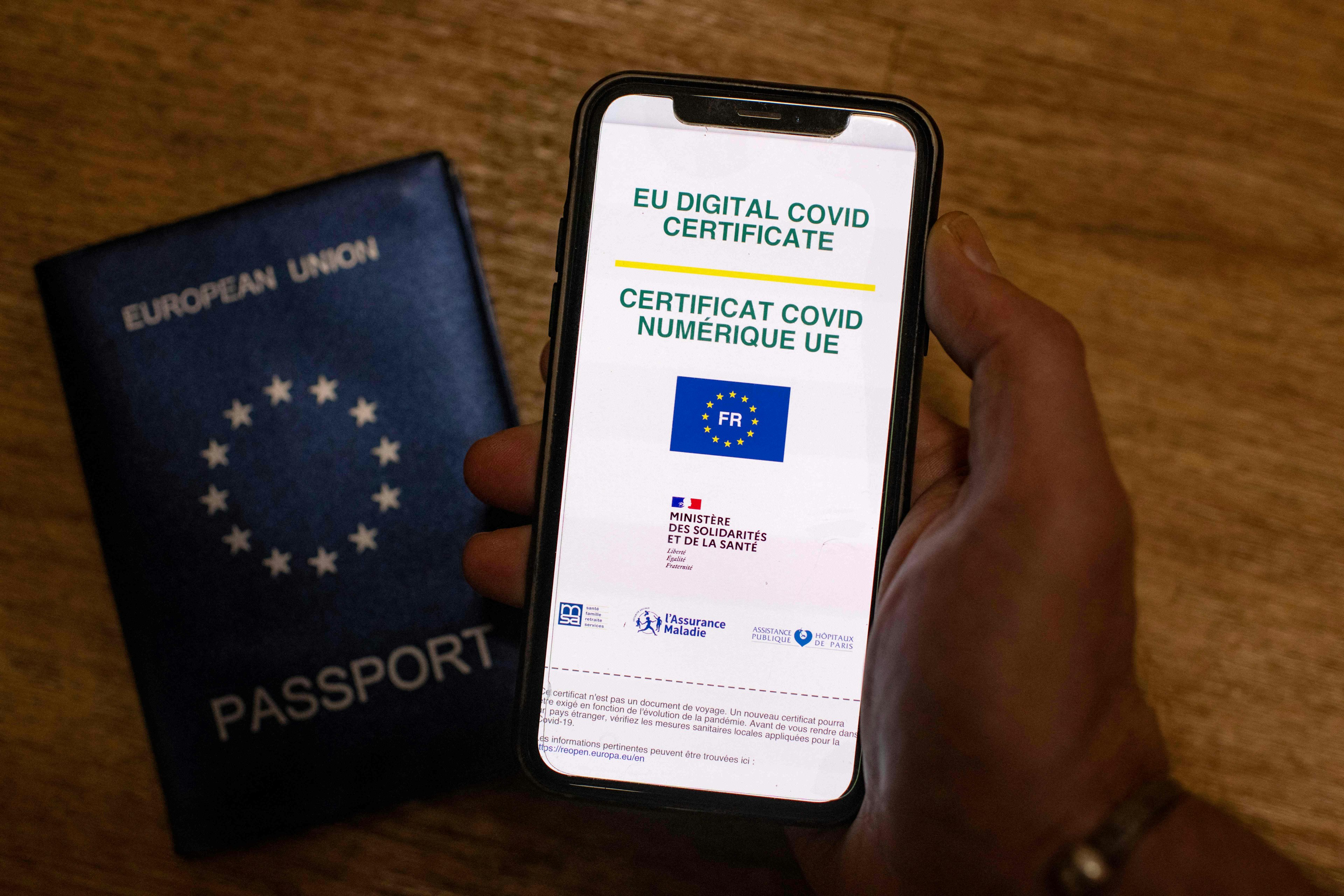 A picture taken on June 29, 2021 in Paris shows a passeport behind a mobile phone whose screen bears a EU Digital Covid certificate