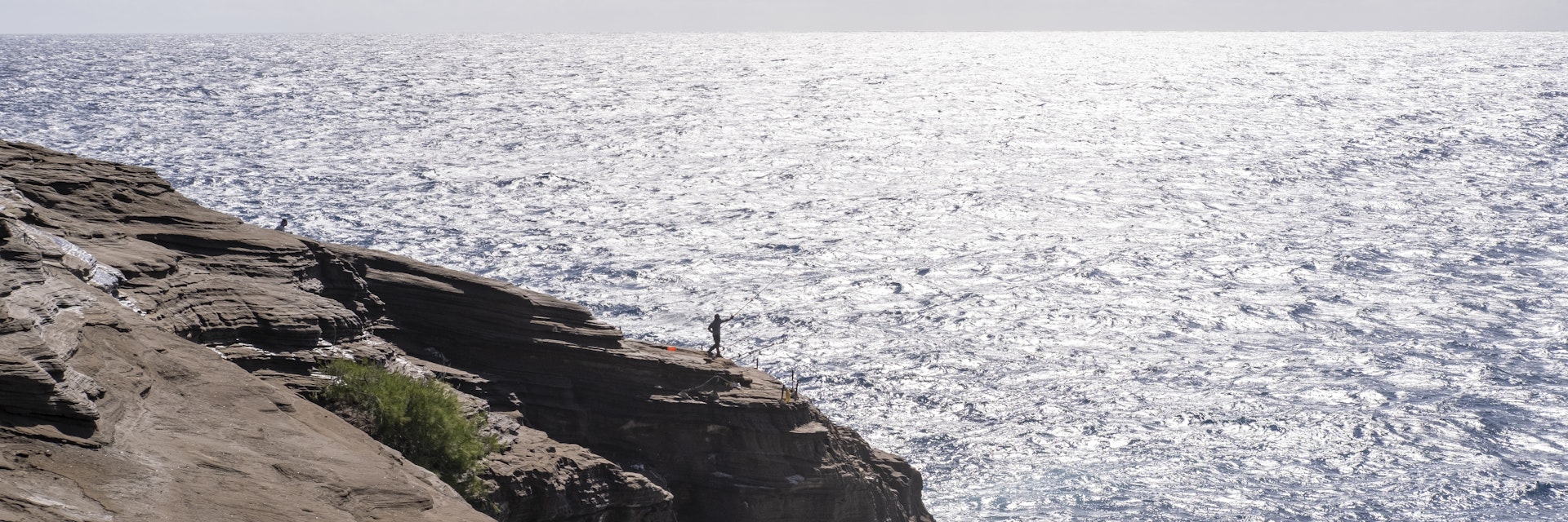 There is a fisherman about to cast his line in the water over a tall cliff. Spitting Caves Hawaii is a hidden gem of East Oahu.