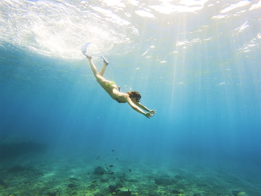 A woman dives into the clear blue sea in the Cyclades islands