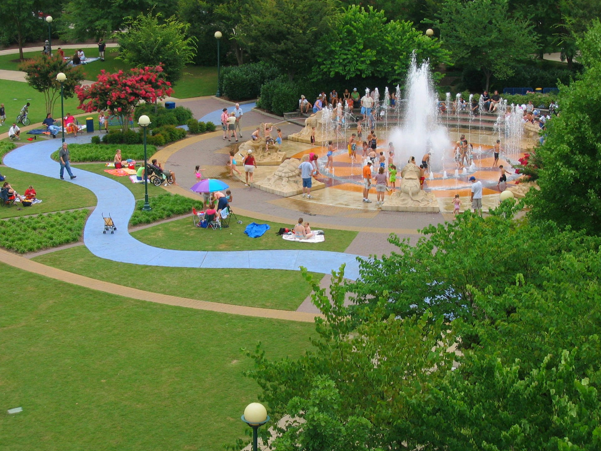 An aerial shot of a park with people playing in a fountain 