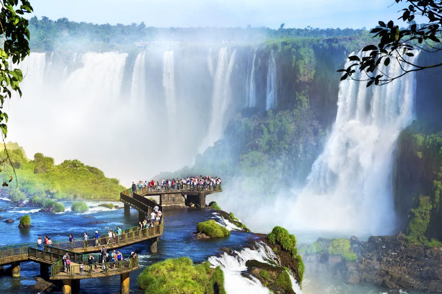 People standing on a wooden boardwalk looking at Iguazú Falls, on the border of Argentina and Brazil