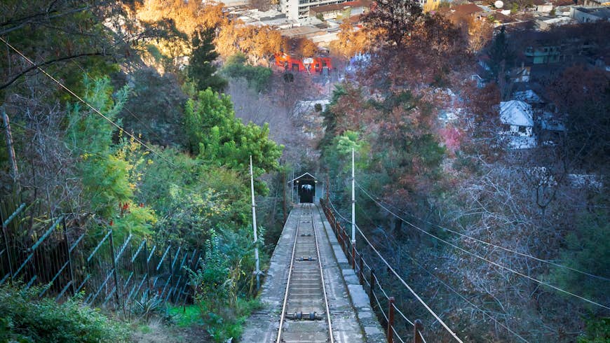 Una línea de tranvía atraviesa el bosque en la cima de la colina de San Cristóbal en Santiago, Chile, que corre al fondo.