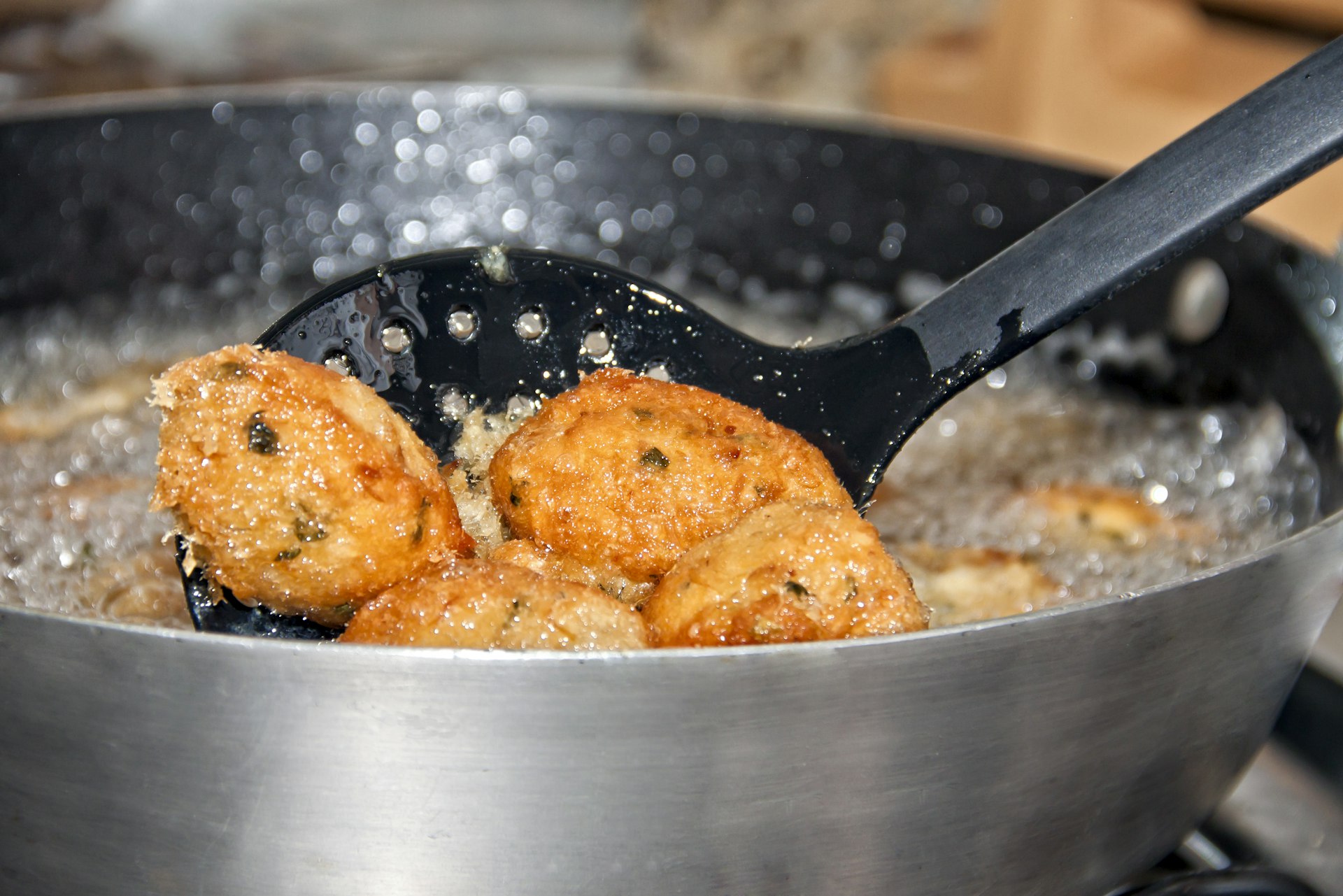 Three codfish balls, known as Bolinho de Bacalhau in Brazil, are fried in a black frying pan with plenty of hot oil in São Paulo.