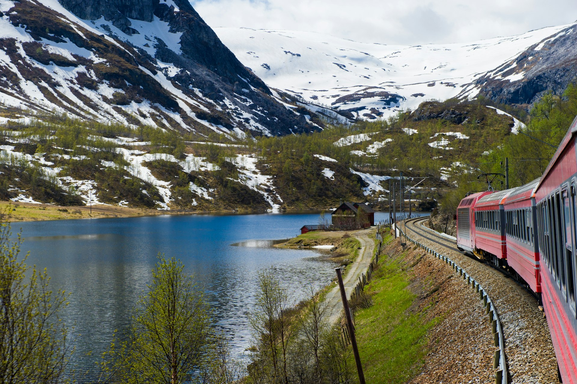 Train passes snow-capped mountains and a river from Oslo to Bergen in Norway.