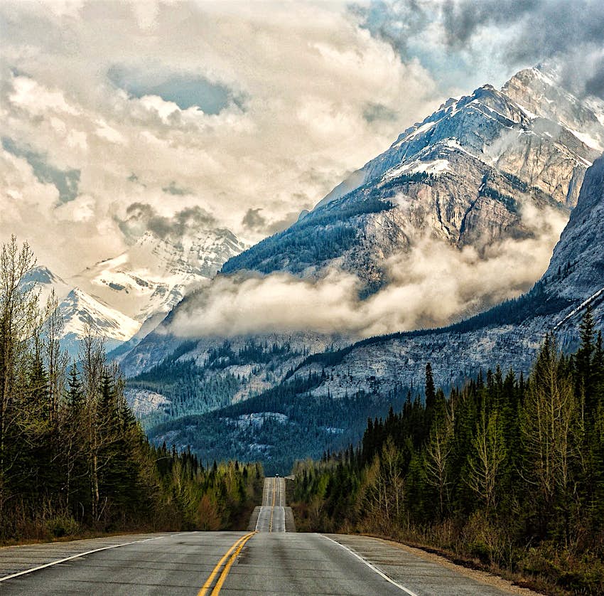An empty road dips and dives towards a cloud smothered mountain in the Canadian Rockies