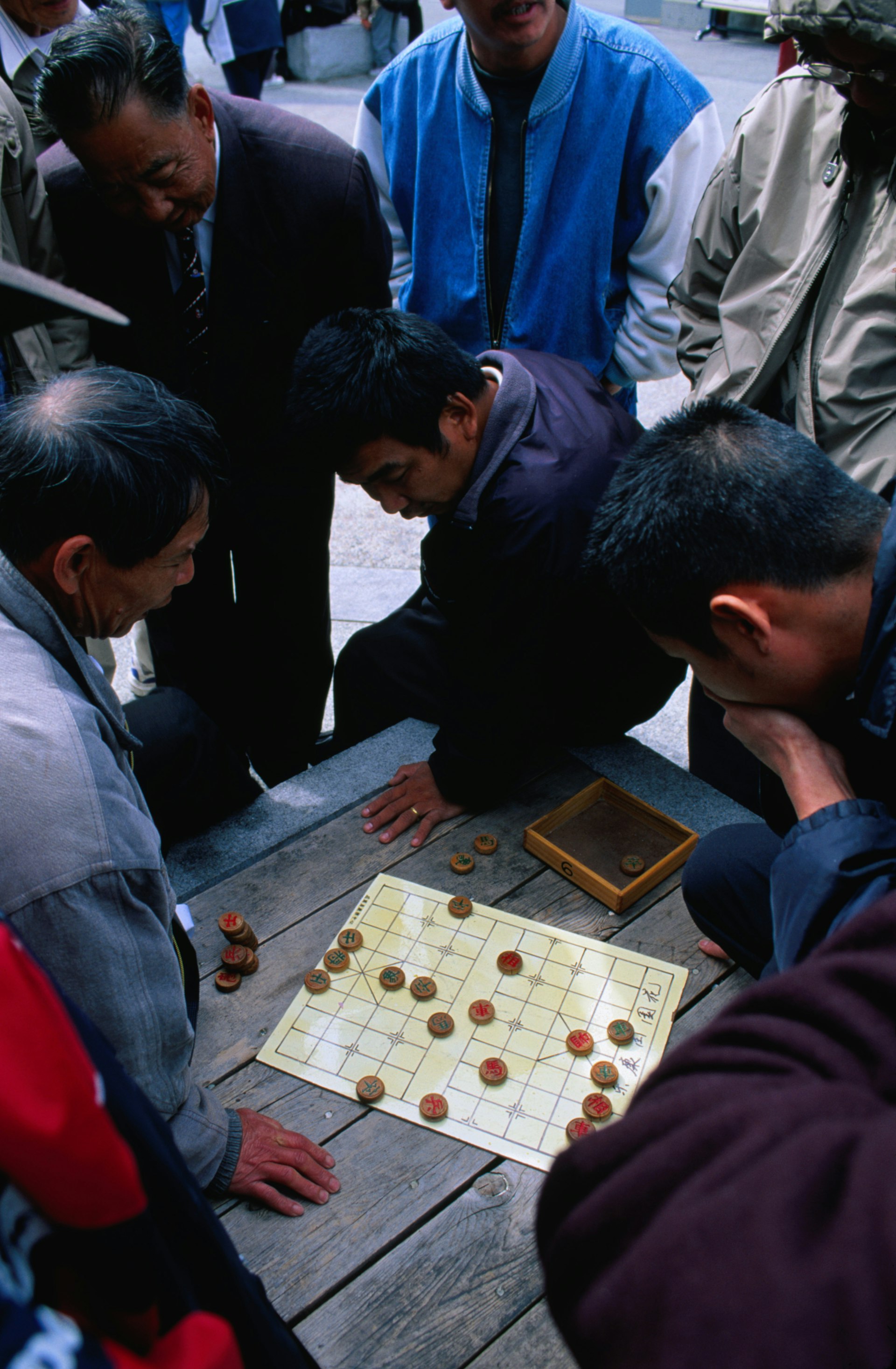 A group of men crowding around a game of Chinese chess at Portsmouth Square in Chinatown, San Francisco