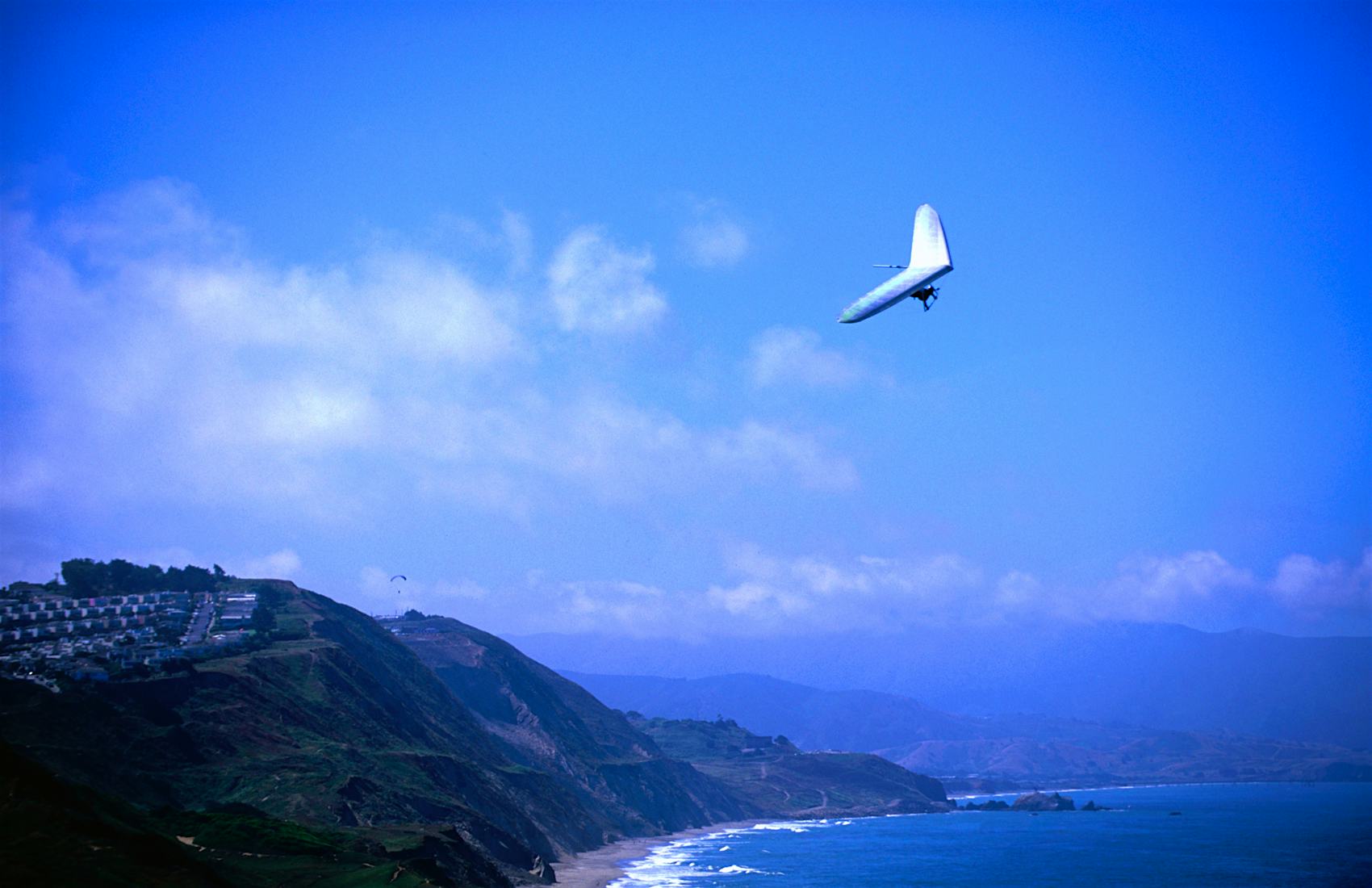 A hang glider swirls over the hills and waters of Fort Funston like a swallow.
