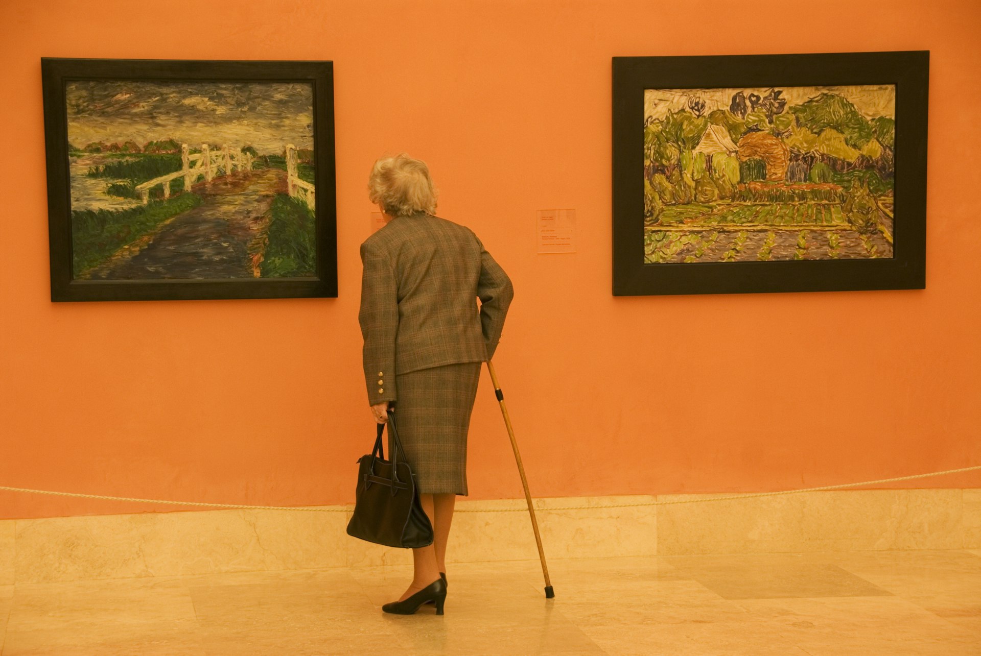 An elderly woman in a suit and with a cane admires two paintings (one by Vincent van Gogh) at Museo Thyssen-Bornemisza, Madrid, Spain
