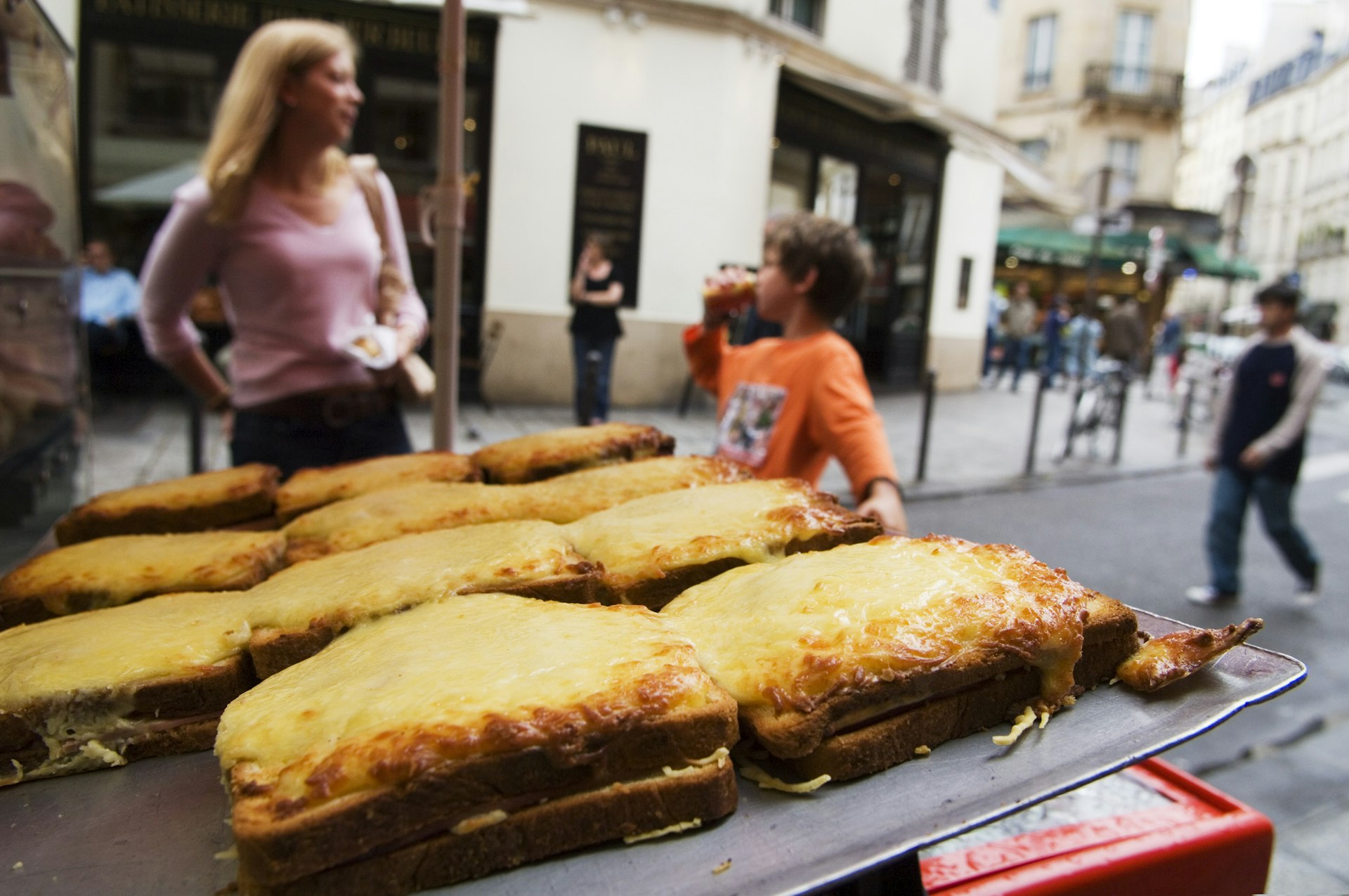A display of croques (toasted cheese sandwiches) on sale on the street in Place St-Germain des Pres area with people in soft focus in the background.