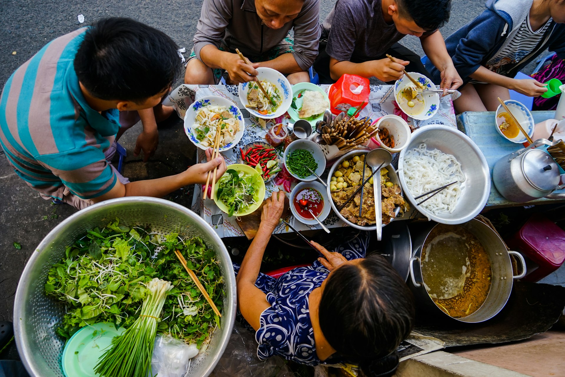 An aerial shot of several people gathered around a slim outside table eating street food in Ho Chi Minh City, Vietnam 