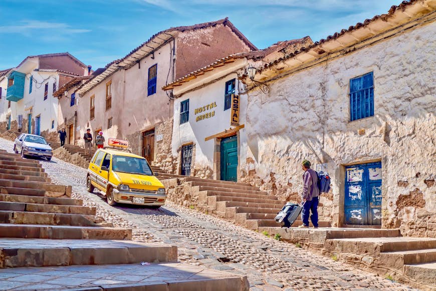 A taxi drives down a steep, cobbled street in the historic center of Cusco. The buildings lining the streets have been converted into quaint hotels.