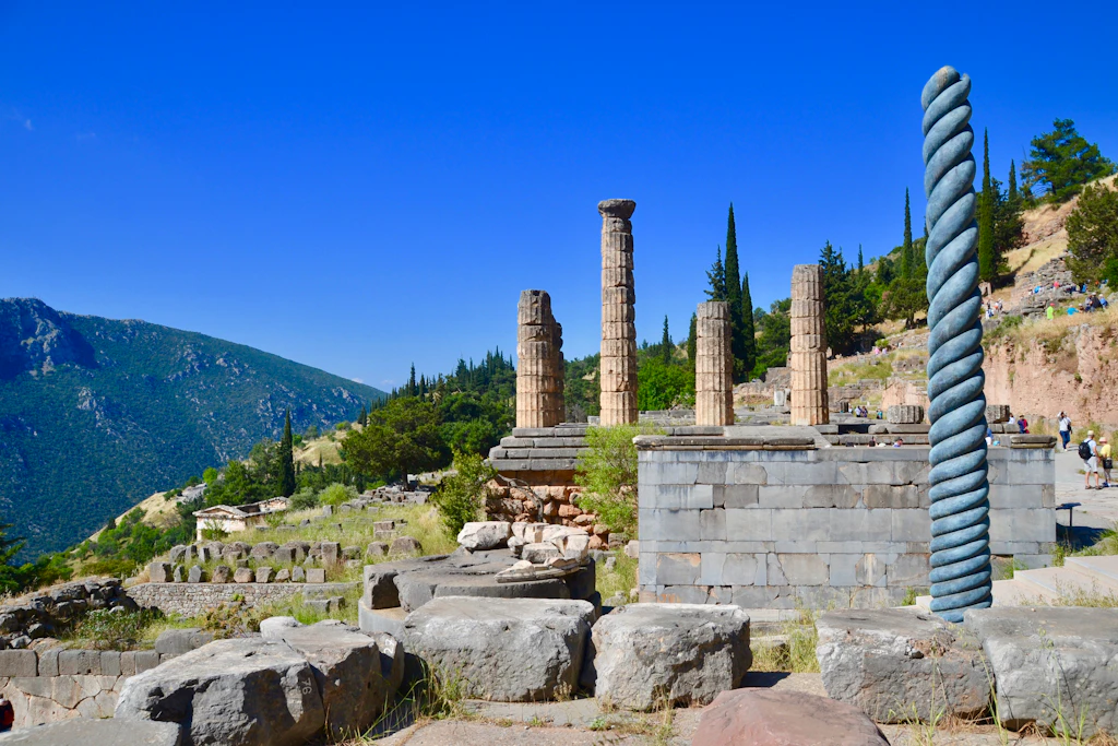 Serpent Column, Delphi Greece A view of the Serpent Column in Delphi with the remaining white columns of the Temple of Apollo behind it.