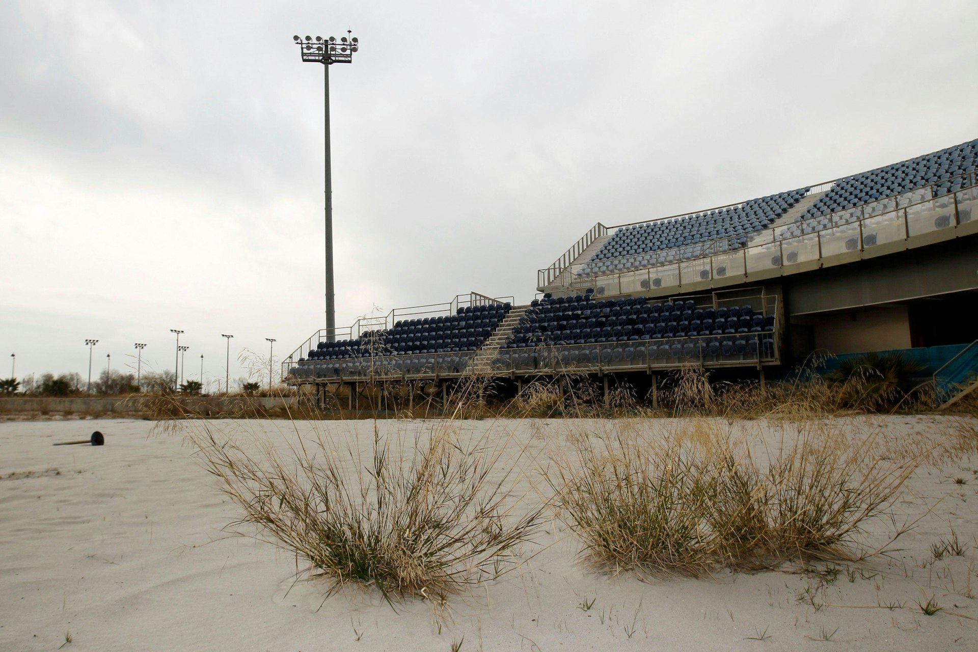 A abandoned Olympic stadium has grass growing in front. 
