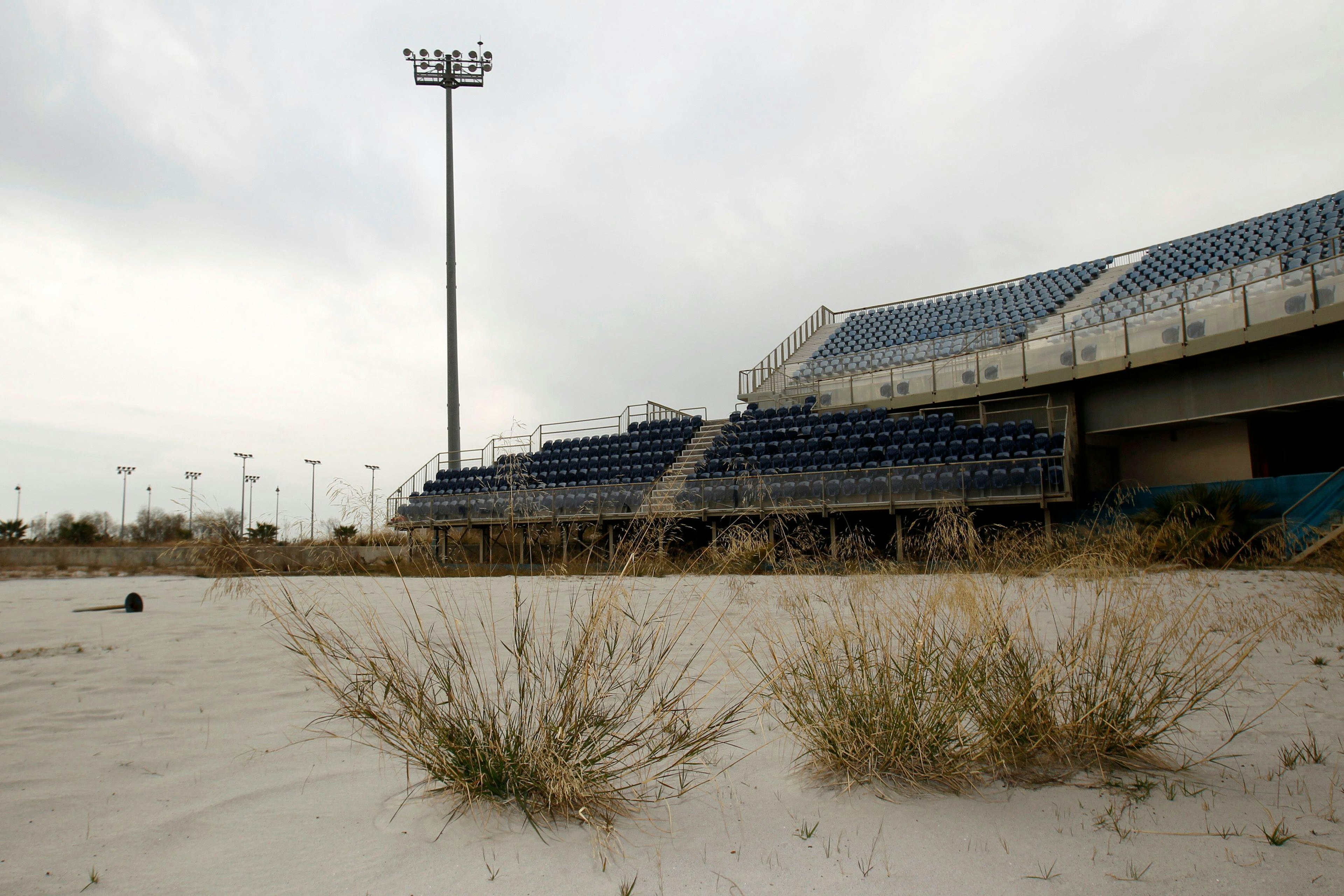 A abandoned Olympic stadium has grass growing in front.