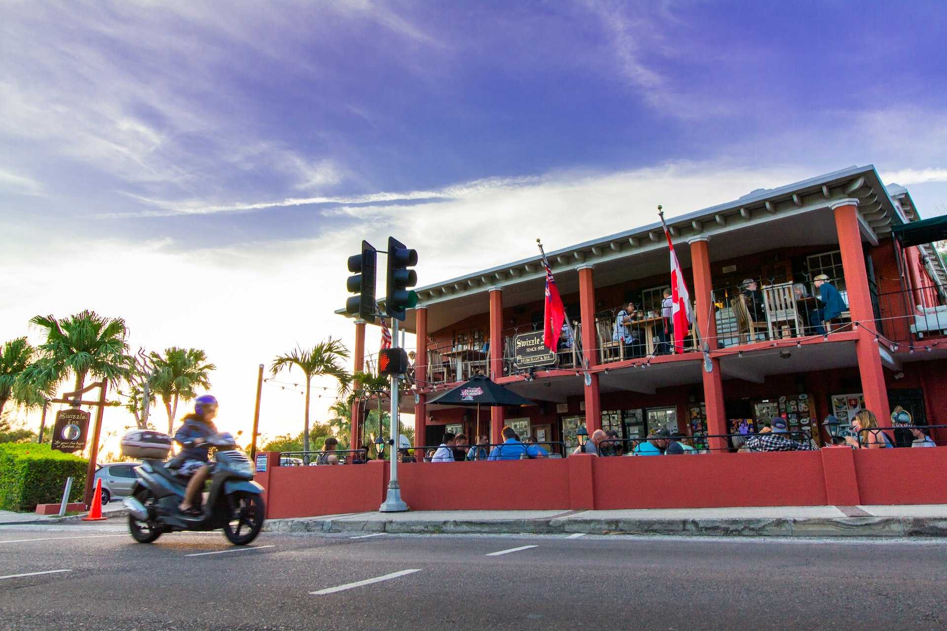 The Swizzle Inn Pub and Restaurant in Bermuda, a roadside pub with people sat at tables on the balcony and at ground-level 