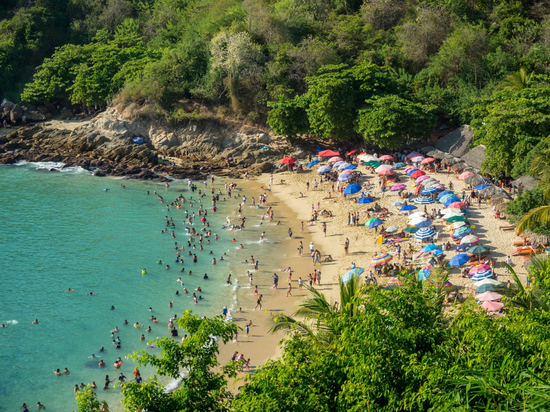 Aerial view of a crowded beach surrounded by jungle, facing turquoise water