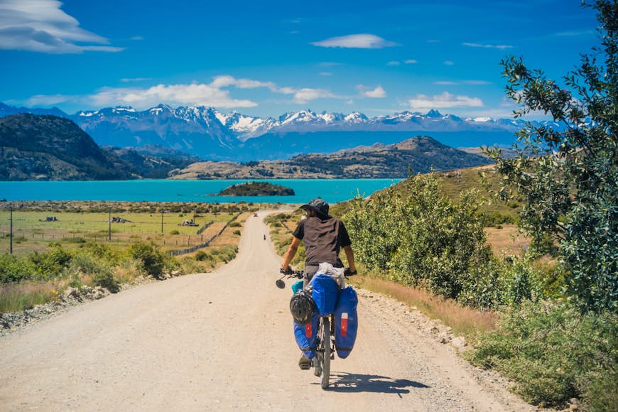 Un recorrido masculino en bicicleta por el camino de terracería de la Carretera Austral, rumbo al Lago Azul y Montañas Grises.