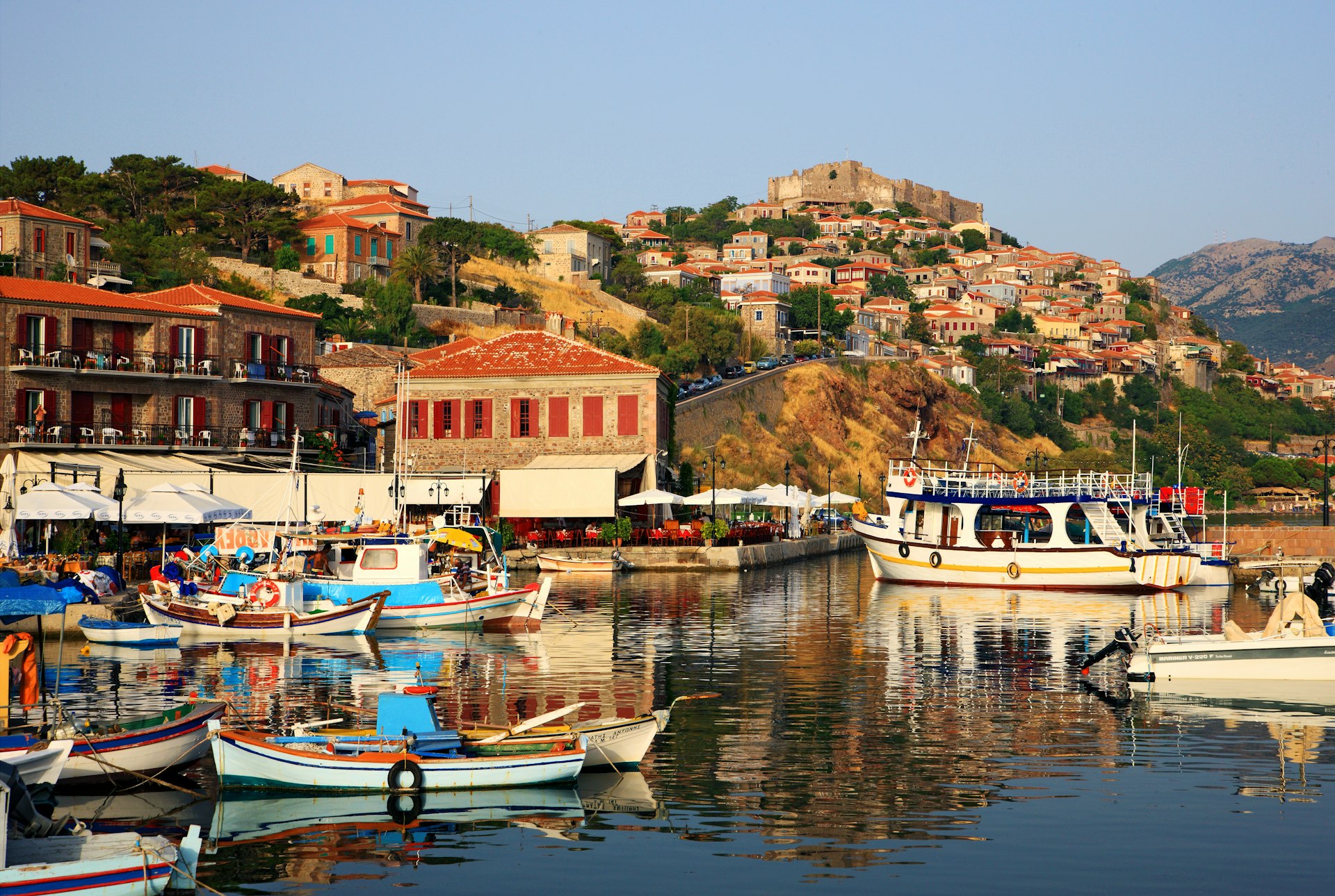 The harbour of Molyvos town and its castle on top of the hill. A number of fishing boats are moored in the harbour.