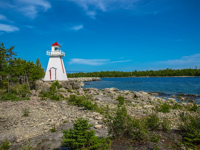 The white and red South Baymouth Range Lighthouse stands next to the water's edge at Lake Huron, Manitoulin Island during the day.