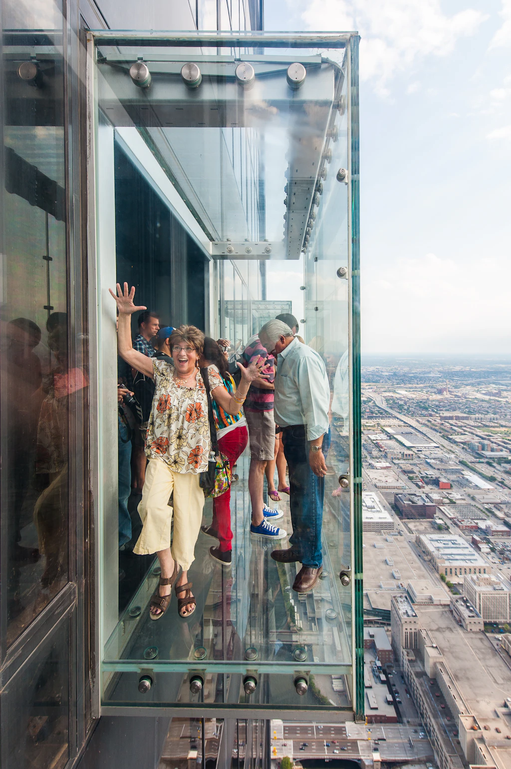 People standing in a glass box on the edge of a skyscraper. 