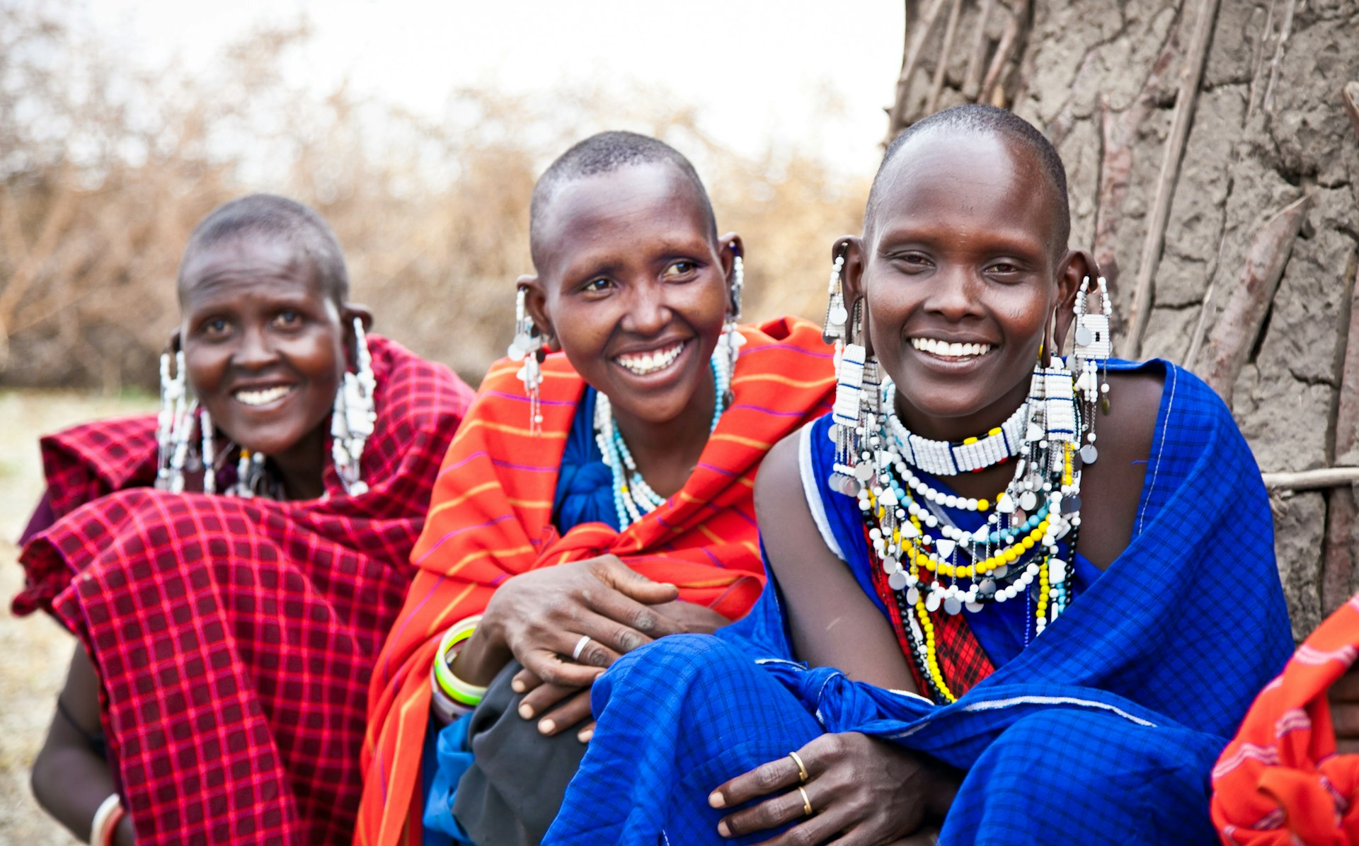 Three Maasai women with traditional robes and ornaments of blue, red and pink stripes at the Serengeti National Park