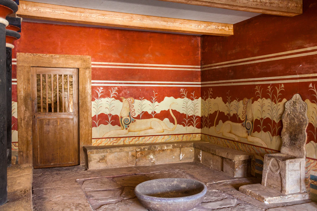 shutterstockRF_213825256.jpg King's chamber of legendary Knossos palace, Crete, Greece. The room is large with red walls and a throne-like chair in the centre of it.