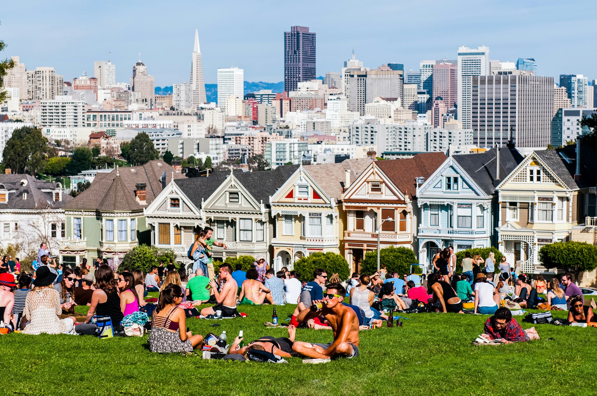 People sit on the grass at Alamo Square Park in San Francisco, next to a series of houses painted in bright colors called the Painted Ladies.