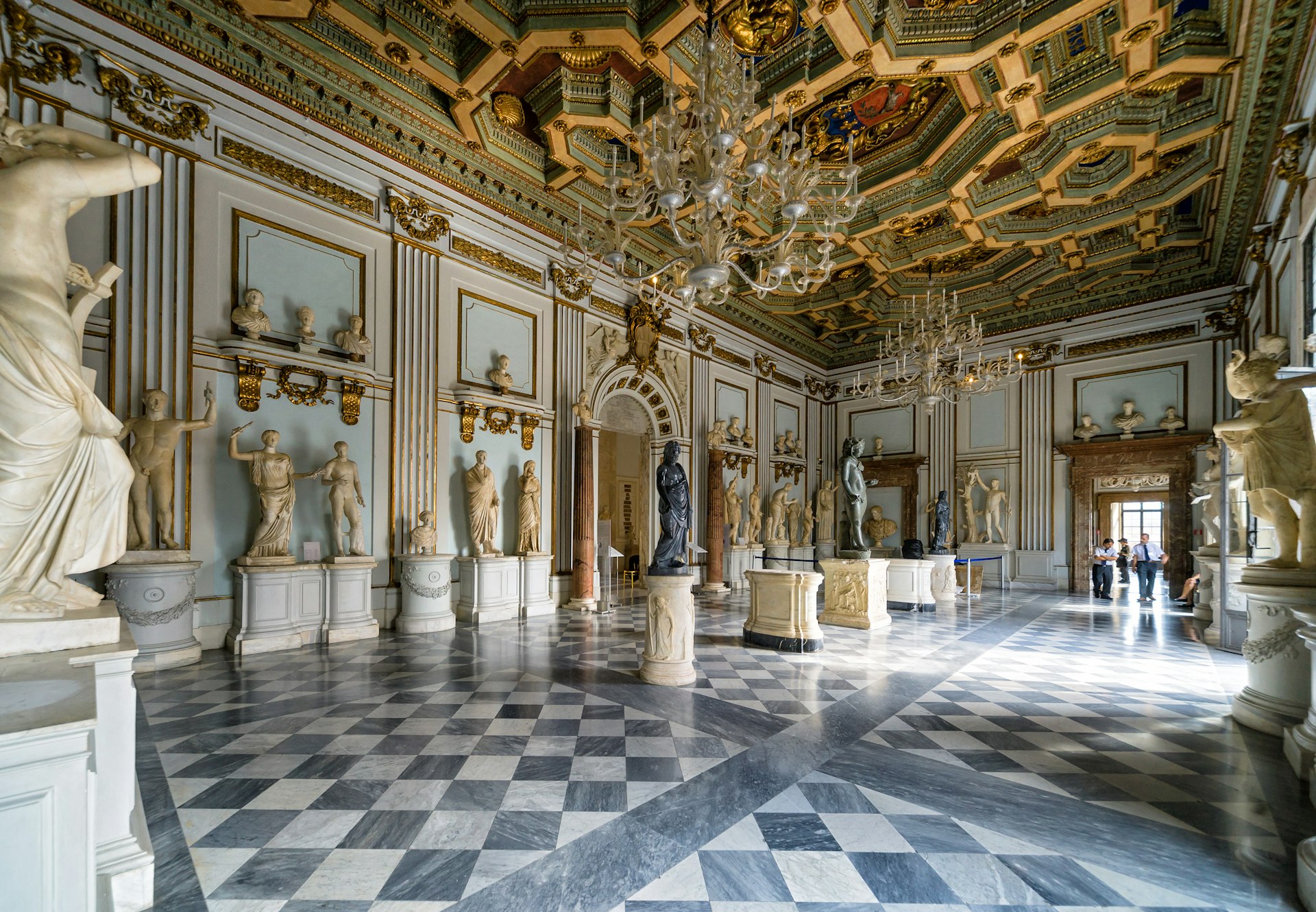 A room with a black-and-white tiled floor is lined with marble sculptures