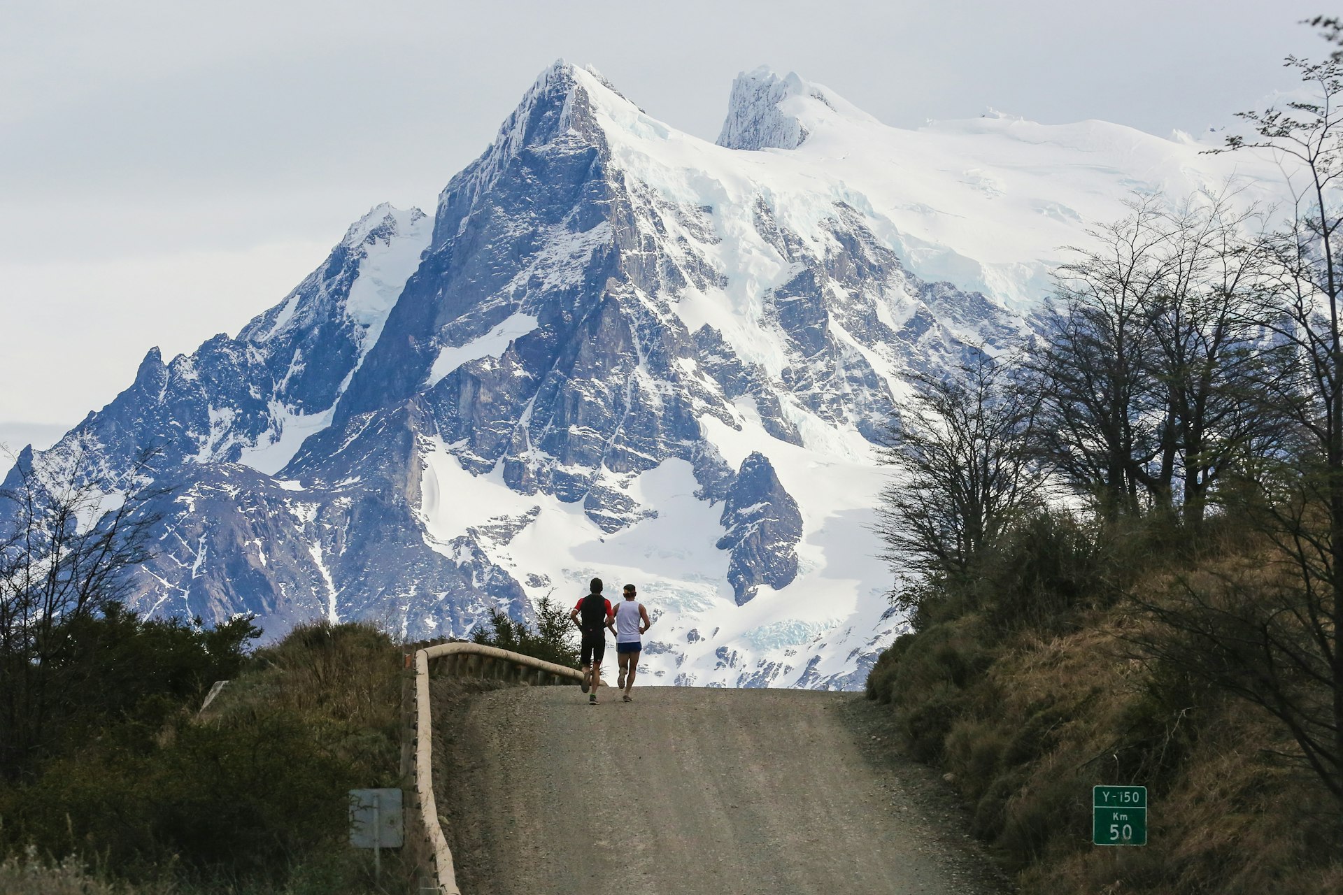 Athletes competing during the Patagonian International Marathon run over the crest of a road, with hulking, snow-capped mountains in the background.