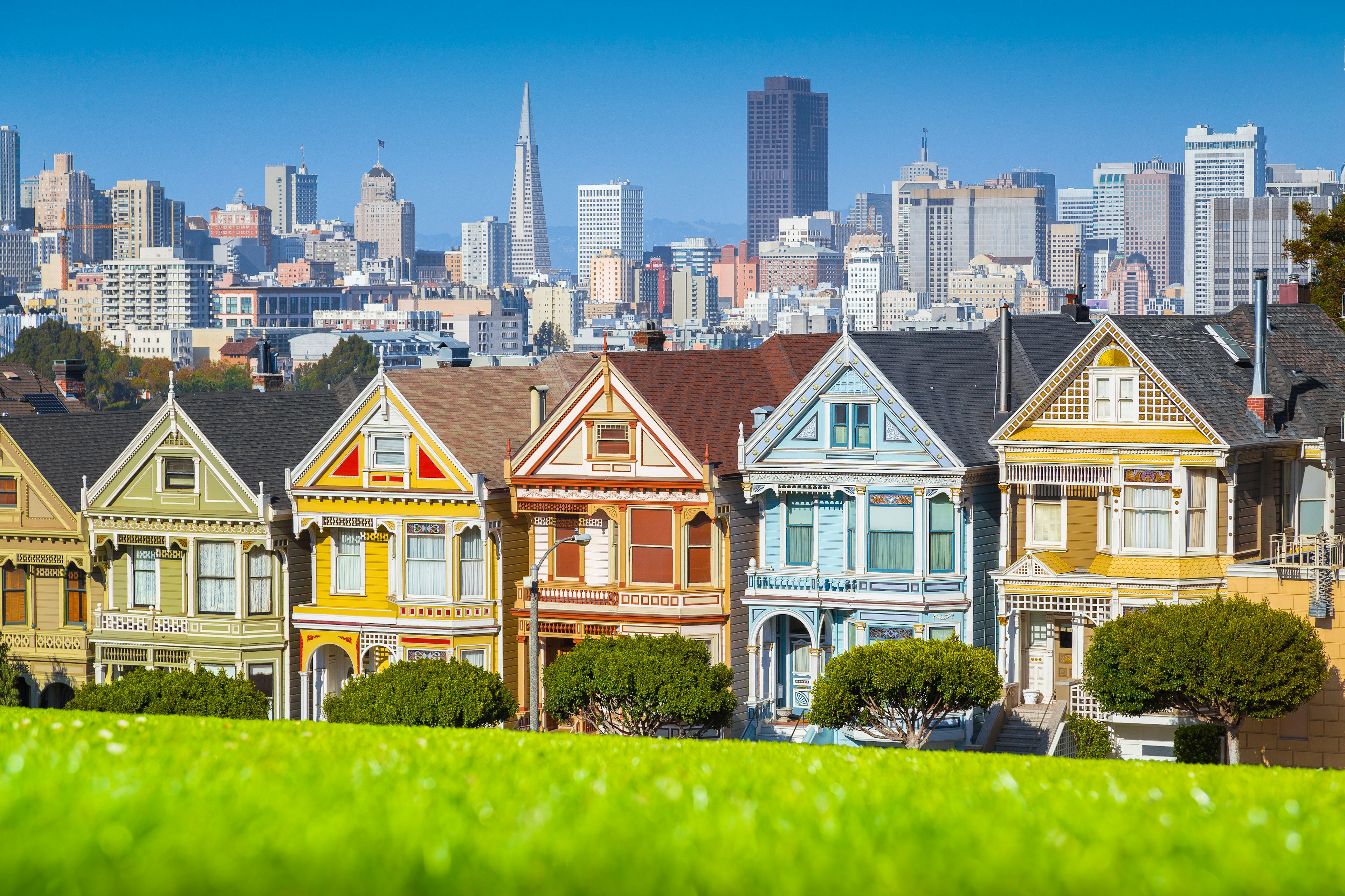 Classic postcard view of famous Painted Ladies, a row of colorful Victorian houses at scenic Alamo Square, with San Francisco skyline in the background on a beautiful sunny day with blue sky in summer