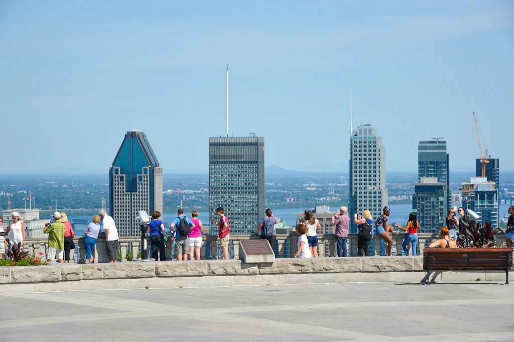 A row of people stand at a viewpoint looking towards a city skyline