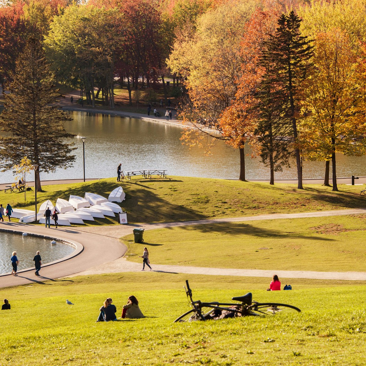 October 18, 2017: Visitors seated on the grass around a lake in Mont Royal Park during autumn.