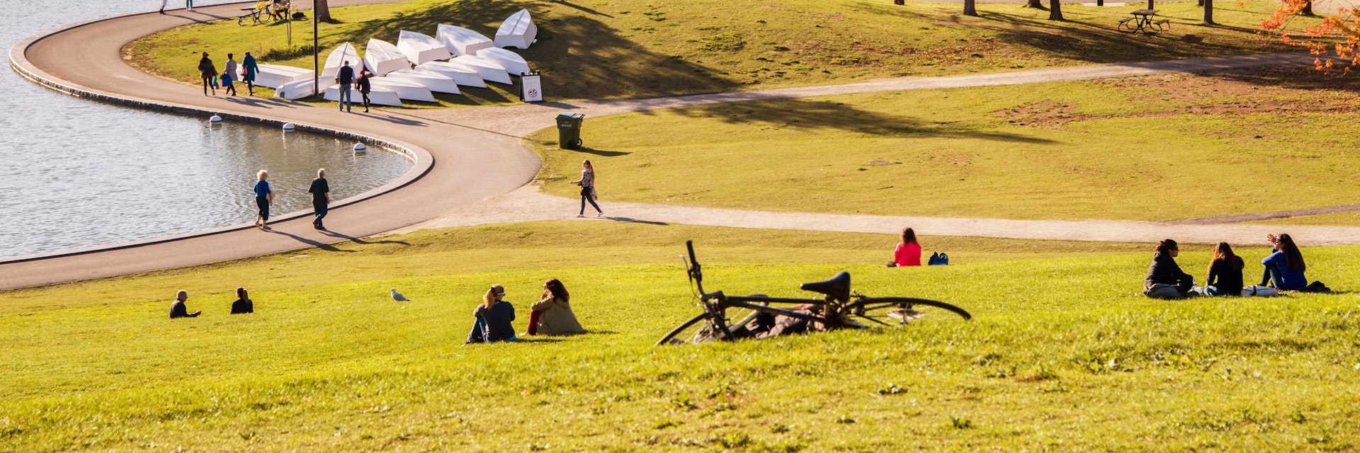 October 18, 2017: Visitors seated on the grass around a lake in Mont Royal Park during autumn.